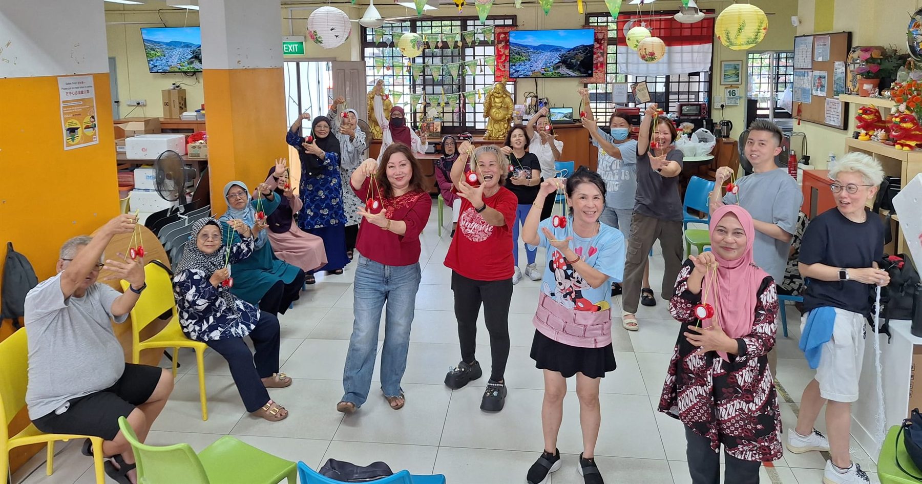 A room full of participants at an active ageing centre, all holding their yoyos up and smiling at the camera